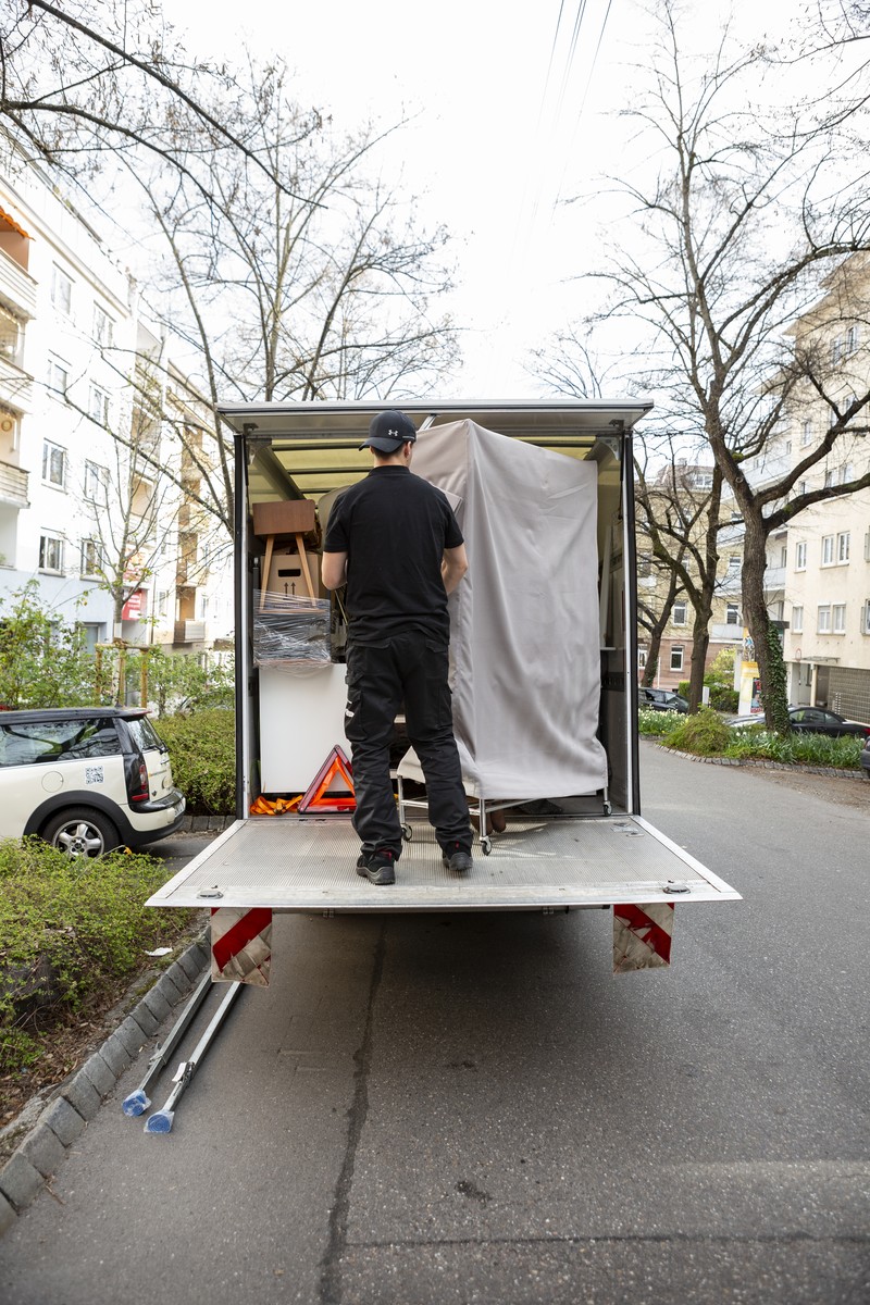 Ein Mitarbeiter verstaut beim Umzug eine Kleiderbox im beladenen Umzugswagen