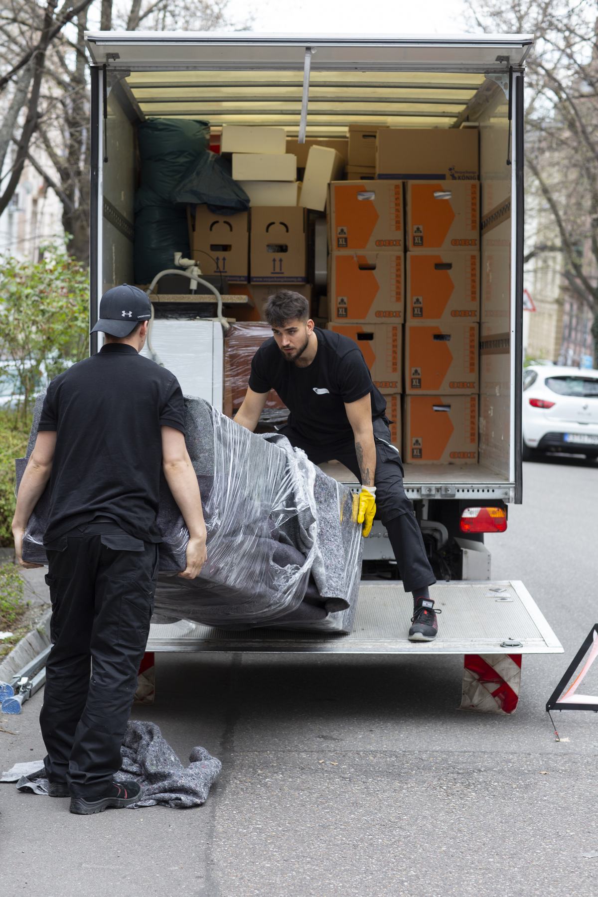 Zwei Mitarbeiter tragen ein eingepacktes Sofa in den Umzugswagen