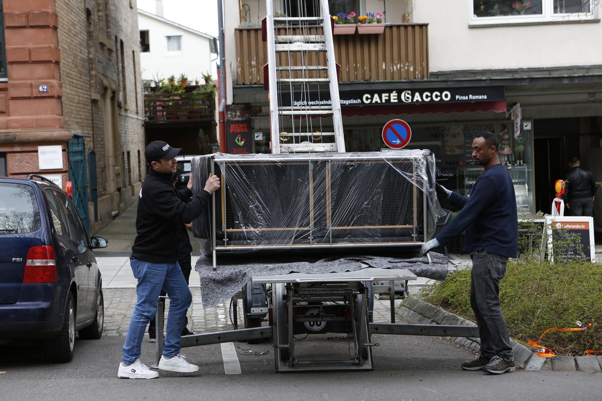 Zwei Mitarbeiter setzen beim Umzug ein eingepacktes Sofa auf die Plattform des Möbellifts