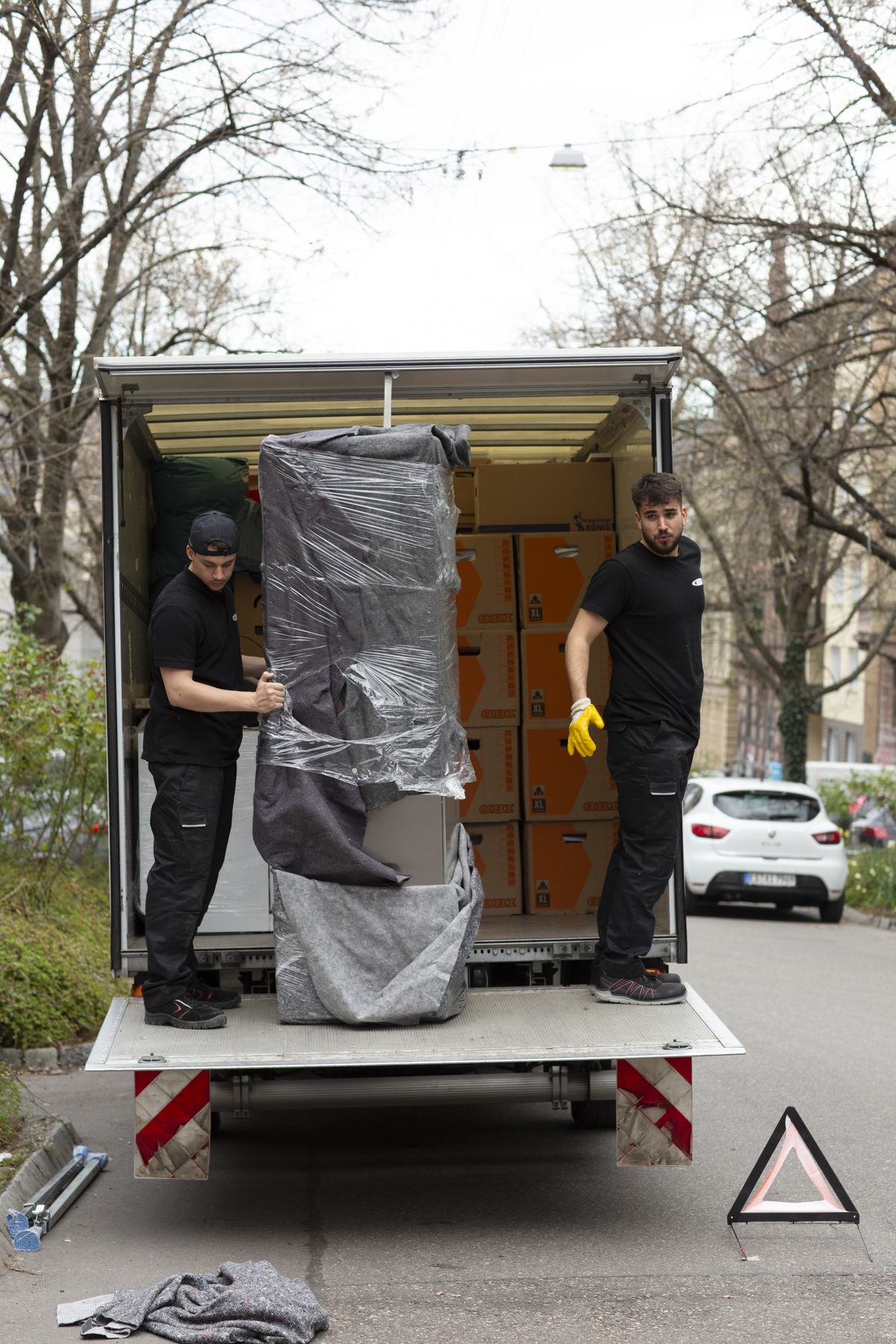 Zwei Mitarbeiter richten ein in Decken und Folie verpacktes Sofa auf der Ladebordwand auf